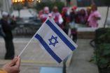 Una persona sostiene una bandera de Israel en primer plano, sobre un fondo difuminado.
