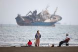 Gente reunida en una playa, mientras se divisa un barco en el estrecho de Ormuz, cerca de la playa de Bandar Abbas.