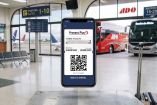 Boleto digital de viaje mostrado en un celular, con una terminal de autobuses y aeropuerto al fondo.