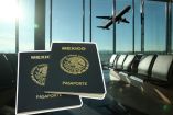 Dos pasaportes mexicanos en primer plano, con un avión despegando al fondo de una sala de espera de aeropuerto.
