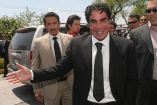 Jorge Kahwagi sonriendo de traje negro durante un evento político, rodeado de colaboradores y equipo de seguridad.
