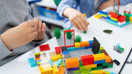 Niños construyen estructuras con bloques de LEGO de distintos colores sobre una mesa.