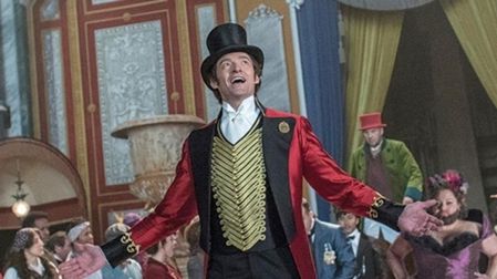Hugh Jackman como P. T. Barnum en El gran showman, con sombrero de copa y saco rojo, rodeado de artistas.