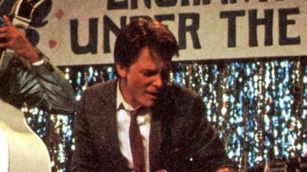 Michael J. Fox como Marty McFly toca una guitarra eléctrica roja durante el baile escolar en Volver al futuro.