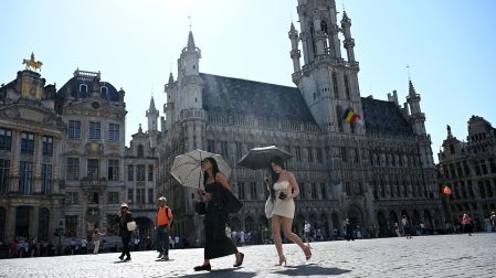 Turistas caminan bajo sombrillas para protegerse del sol mientras visitan la Grand-Place, durante ola de calor en Bruselas
