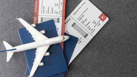Boletos de avión, pasaportes y un avión en miniatura colocados sobre una superficie gris.