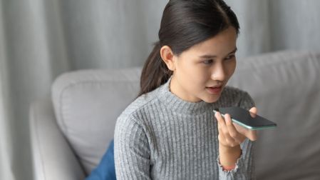 Mujer utiliza el asistente de voz de su celular mediante un comando hablado.