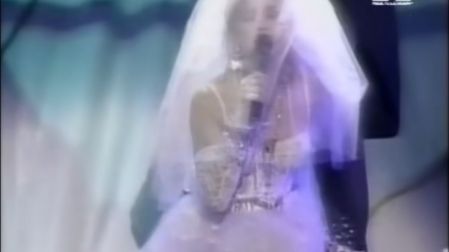 Madonna con vestido de novia, velo blanco y micrófono durante su presentación de Like a Virgin en los premios MTV de 1984.