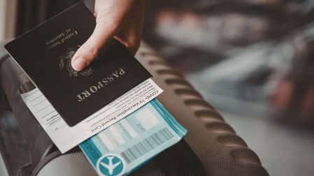 Persona sostiene un pasaporte sobre documentos de viaje y una maleta, para ilustrar la identificación vencida durante un viaje nacional.