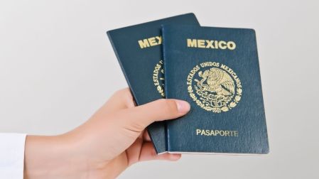 Una mano sostiene dos pasaportes mexicanos de color verde oscuro para ilustrar la identificación durante un viaje nacional.