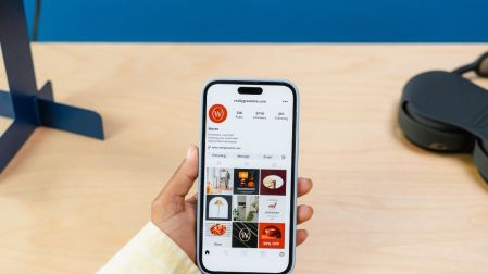 Persona sostiene un celular con un perfil comercial de Instagram abierto y una cuadrícula de publicaciones.