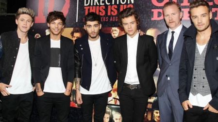 Los cinco integrantes de One Direction, incluido Liam Payne a la derecha, posan junto a un hombre de traje ante un cartel del grupo.