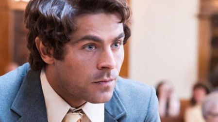 Zac Efron como Ted Bundy en Extremadamente cruel, malvado y perverso, con traje azul y corbata en una sala judicial.