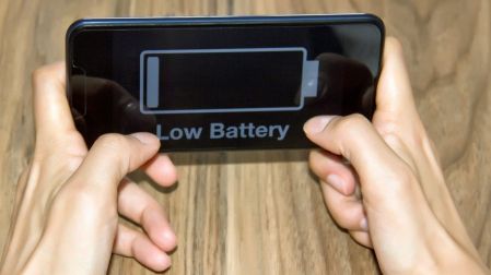 Manos sosteniendo un celular en posición horizontal con un icono de batería casi vacía y el mensaje Low Battery en pantalla.