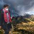 Contraste de Luz y Tormenta sobre un Valle de Montaña. Encima hay una mujer cubierta con ropa abrigadora y un cubrebocas.