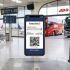 Boleto digital de viaje mostrado en un celular, con una terminal de autobuses y aeropuerto al fondo.