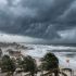 Fuerte oleaje y vientos intensos golpeando una zona costera durante el acercamiento de una tormenta tropical, con cielo oscuro y palmeras doblándose por las ráfagas.