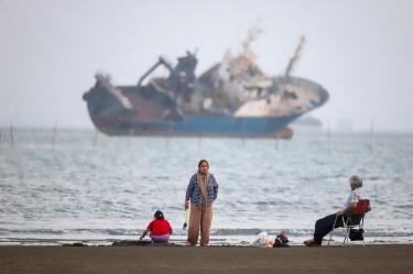 Gente reunida en una playa, mientras se divisa un barco en el estrecho de Ormuz, cerca de la playa de Bandar Abbas.