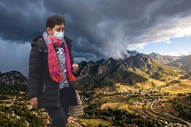 Contraste de Luz y Tormenta sobre un Valle de Montaña. Encima hay una mujer cubierta con ropa abrigadora y un cubrebocas.