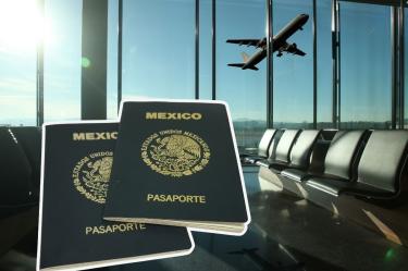 Dos pasaportes mexicanos en primer plano, con un avión despegando al fondo de una sala de espera de aeropuerto.